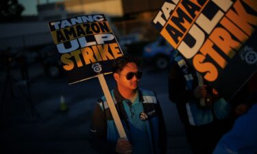 Amazon delivery trucks pass people holding signs and marching during a strike by Teamsters union members at an Amazon facility in Alpharetta