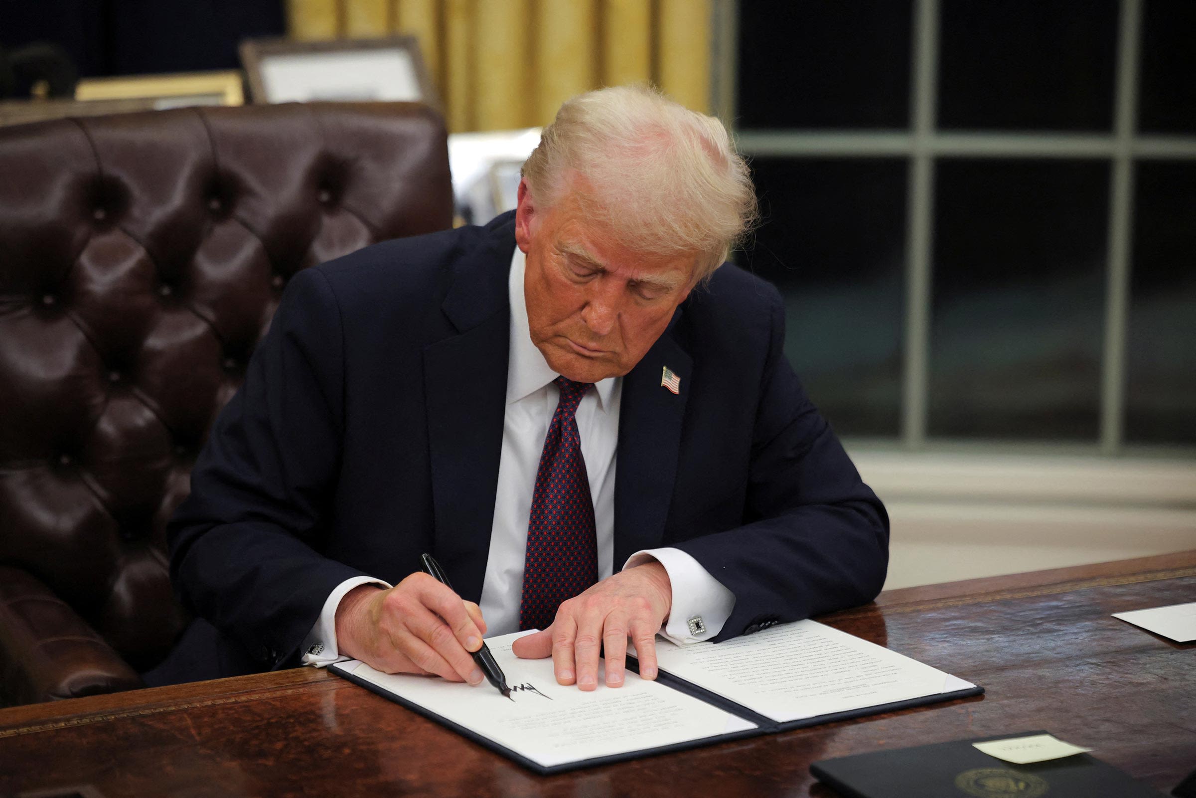 <i>Carlos Barria/Reuters via CNN Newsource</i><br/>President Donald Trump signs documents as he issues executive orders and pardons for January 6 defendants in the Oval Office at the White House on Inauguration Day in Washington