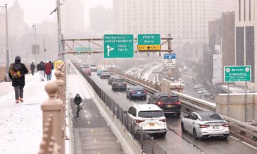 People walk along the Brooklyn Bridge as cars drive into Manhattan on January 6 in New York City.