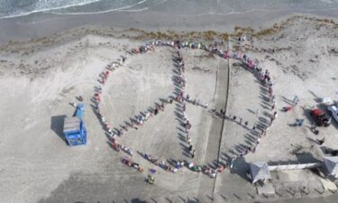 Neighbors gather on the beach near Horace Caldwell Pier to make the outline of a giant peace sign