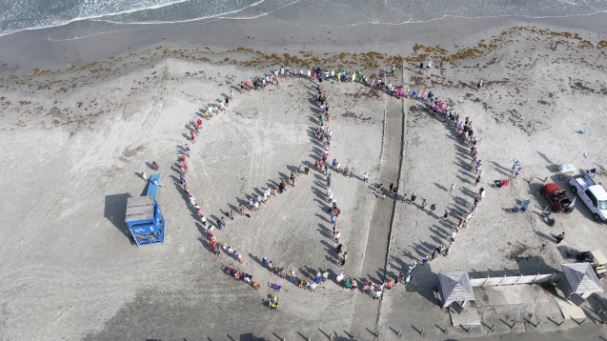 <i>Bryan Hofmann/KRIS via CNN Newsource</i><br/>Neighbors gather on the beach near Horace Caldwell Pier to make the outline of a giant peace sign