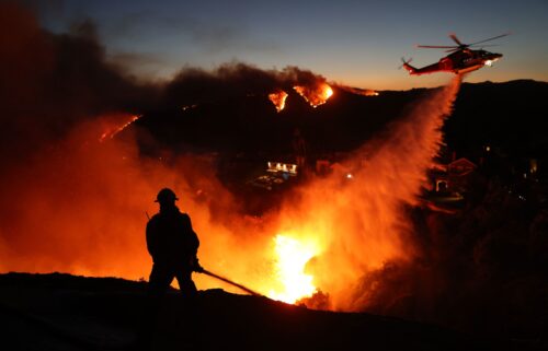 Fire personnel respond to homes destroyed while a helicopter drops water as the Palisades Fire burns on January 7.