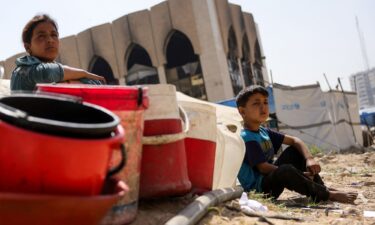 Children sit with plastic buckets as displaced Palestinians collect water in Gaza City. As its expanded military operation continues