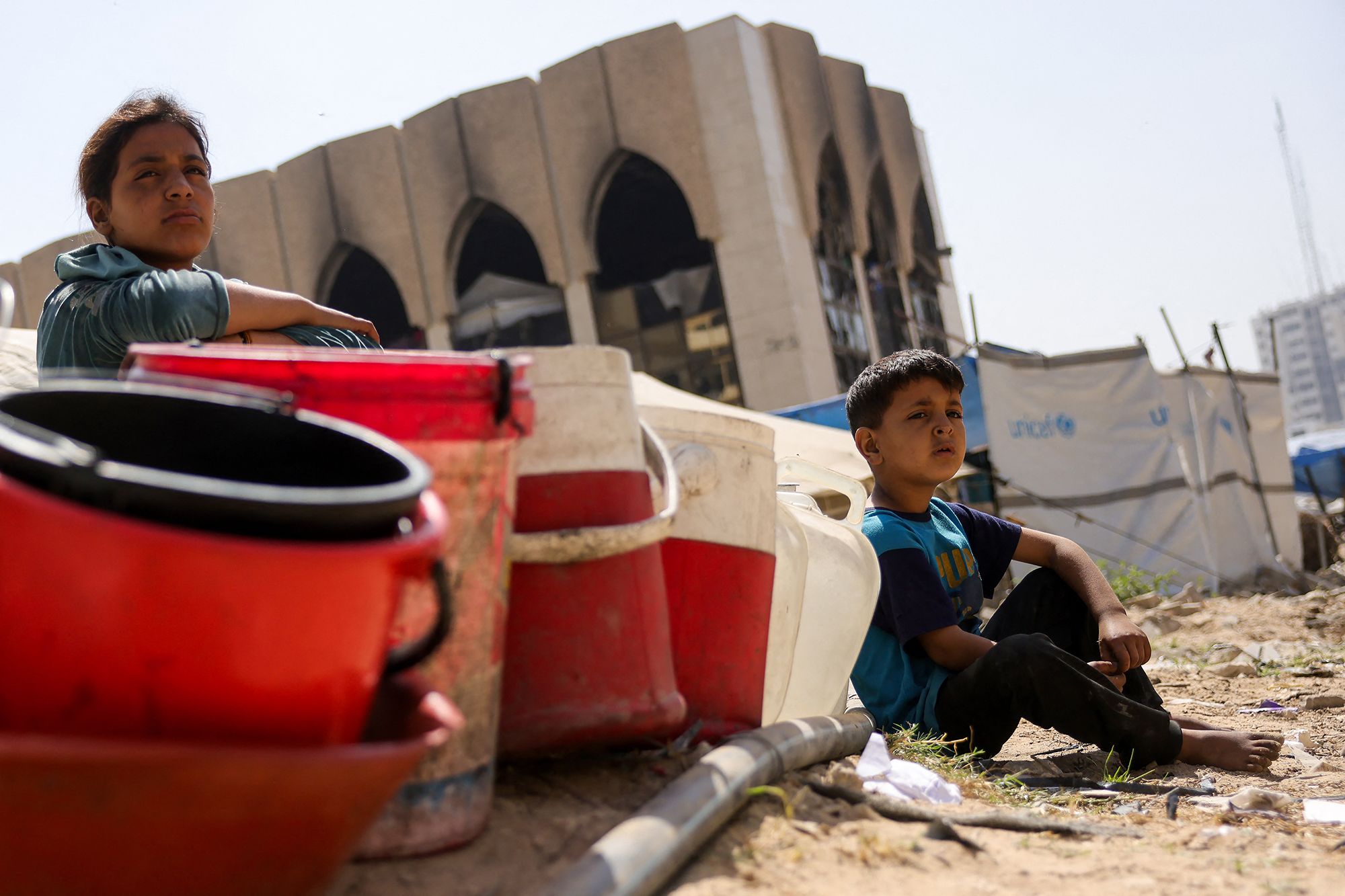 Children sit with plastic buckets as displaced Palestinians collect water in Gaza City. As its expanded military operation continues