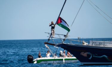 Climate activist Greta Thunberg stands next to a Palestinian flag after boarding the Madleen and before setting sail for Gaza with the Freedom Flotilla Coalition
