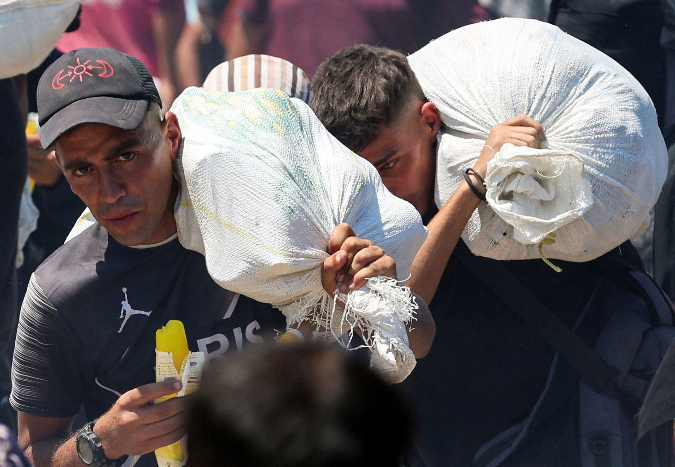 <i>Ramadan Abed/Reuters via CNN Newsource</i><br/>Palestinians seeking aid from the U.S.-backed Gaza Humanitarian Foundation carry bags
