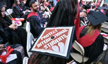 A Harvard University graduate with a message in support of international students on her mortarboard sits with fellow students at the start of commencement exercises at Harvard University in Harvard Yard