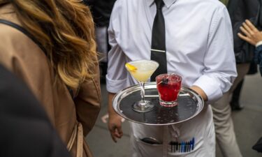 A waiter carries drinks across a sidewalk to an outdoor table in New York City.