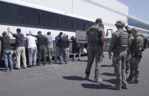 This image from video provided by US Immigration and Customs Enforcement shows manufacturing plant employees waiting to have their legs shackled at the Hyundai Motor Group’s electric vehicle plant