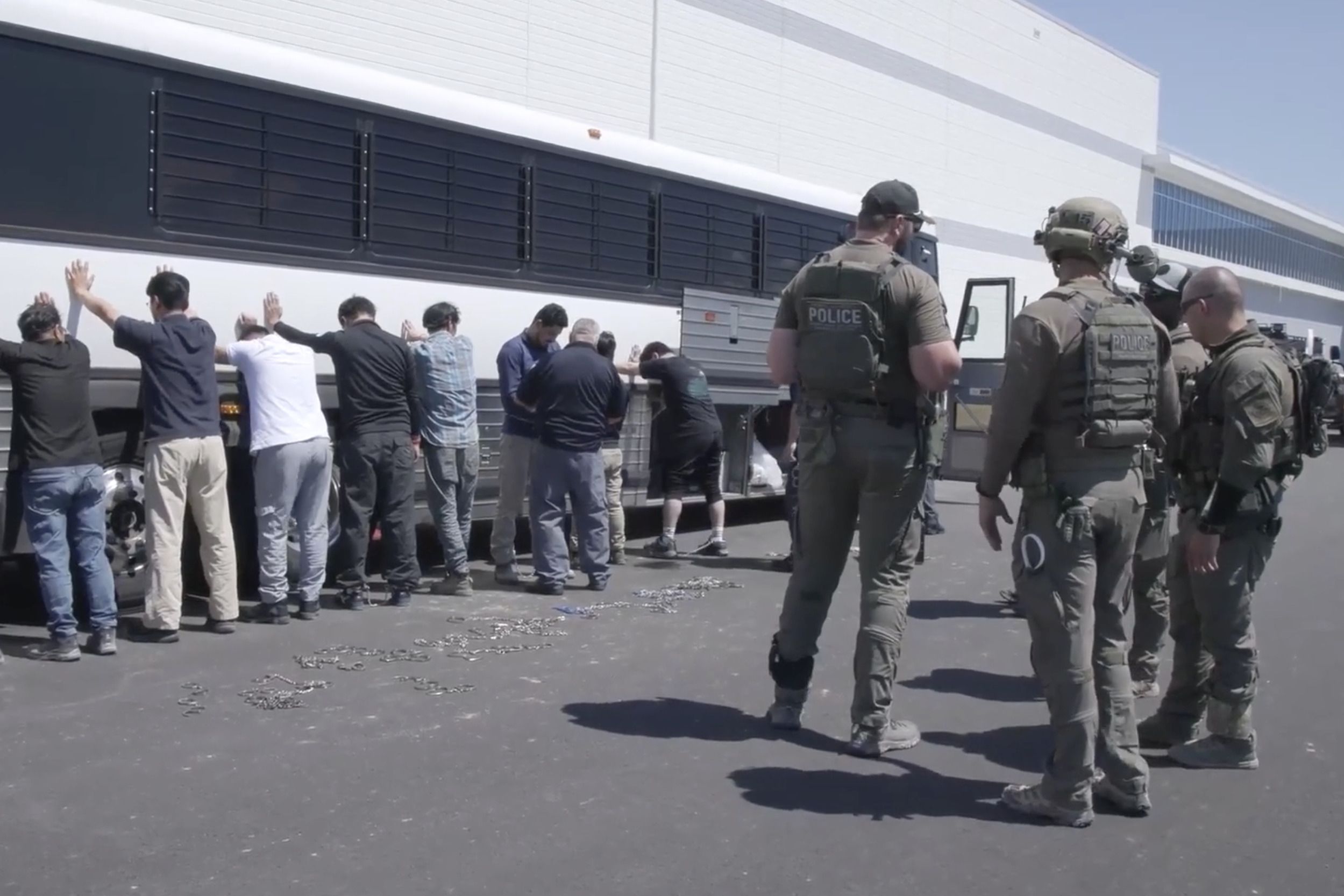 This image from video provided by US Immigration and Customs Enforcement shows manufacturing plant employees waiting to have their legs shackled at the Hyundai Motor Group’s electric vehicle plant