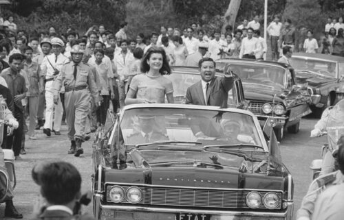 Jacqueline Kennedy and Chief of State Prince Norodom Sihanouk are cheered during a motorcade in Phnom Penh.