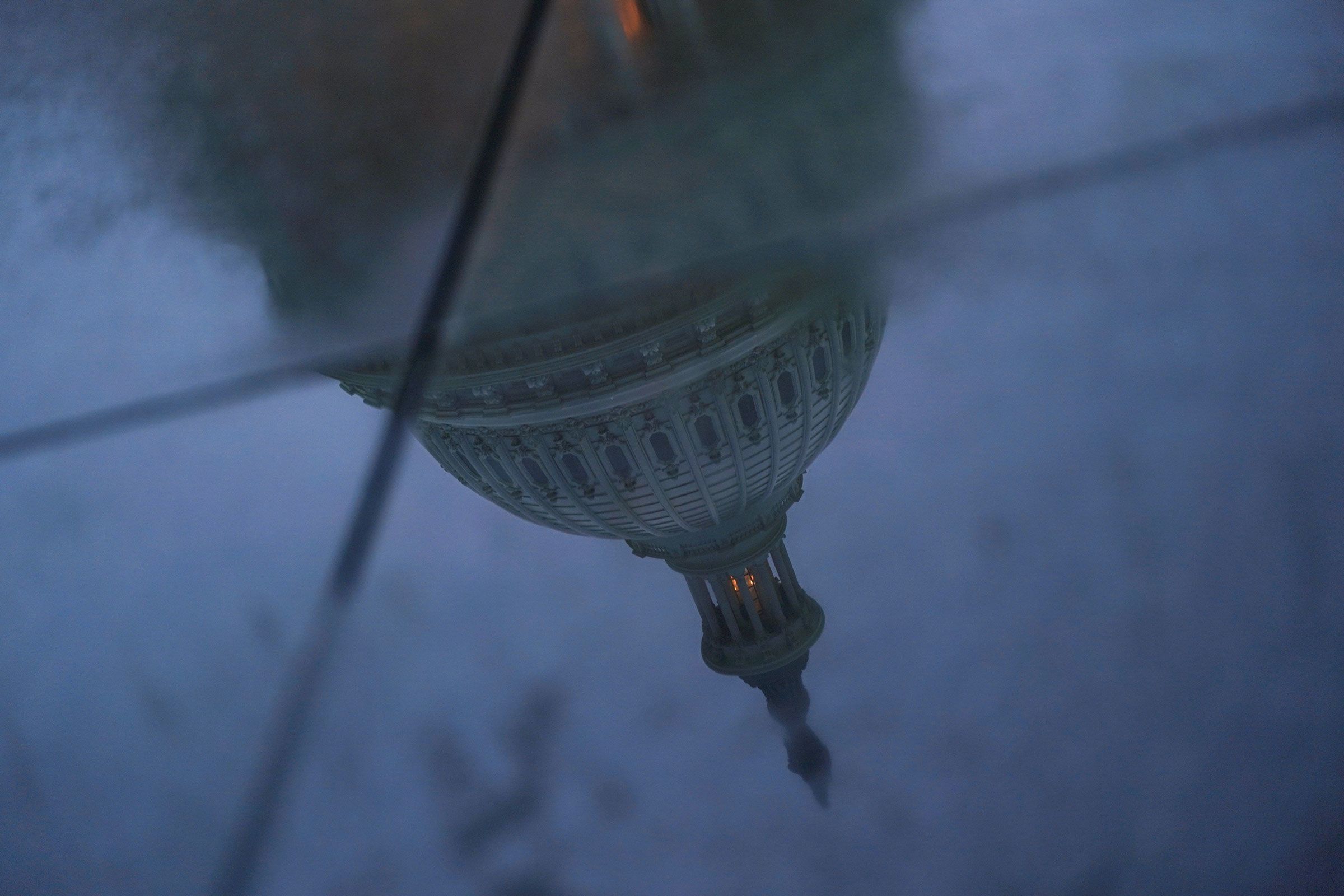 The US Capitol dome is reflected in a puddle on the ground