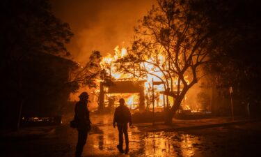 Firefighters watch the flames from the Palisades Fire burning a home on January 8
