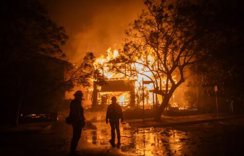 Firefighters watch the flames from the Palisades Fire burning a home on January 8