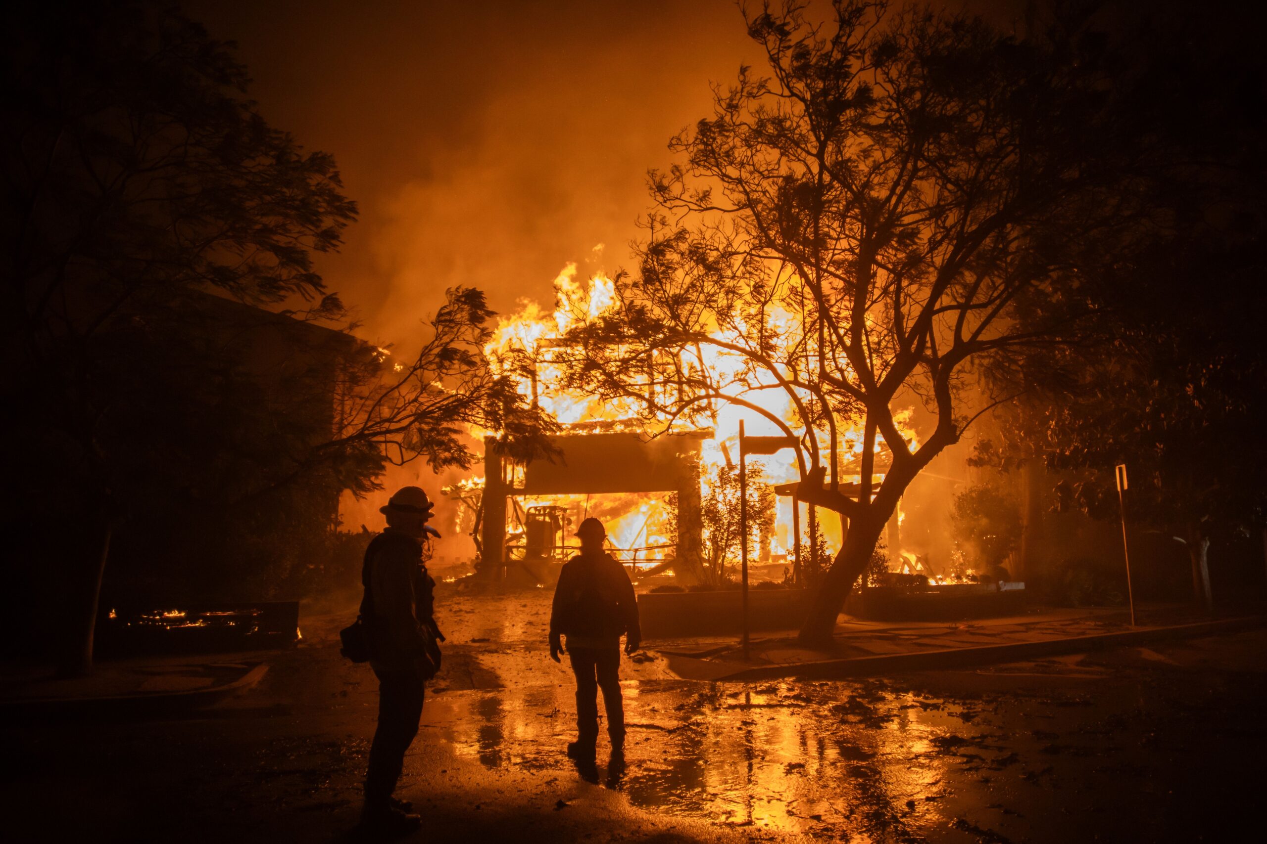 <i>Apu Gomes/Getty Images via CNN Newsource</i><br/>Firefighters watch the flames from the Palisades Fire burning a home on January 8