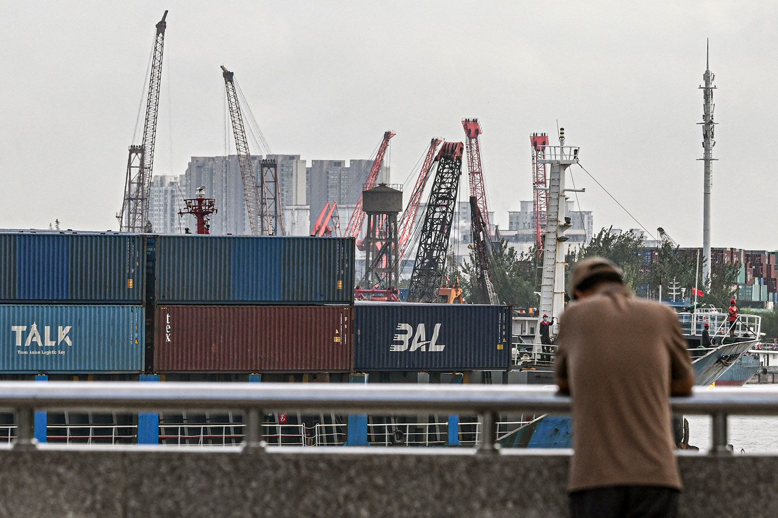 A man stands as a cargo ship carrying containers sails into a dock at a container terminal in Shanghai
