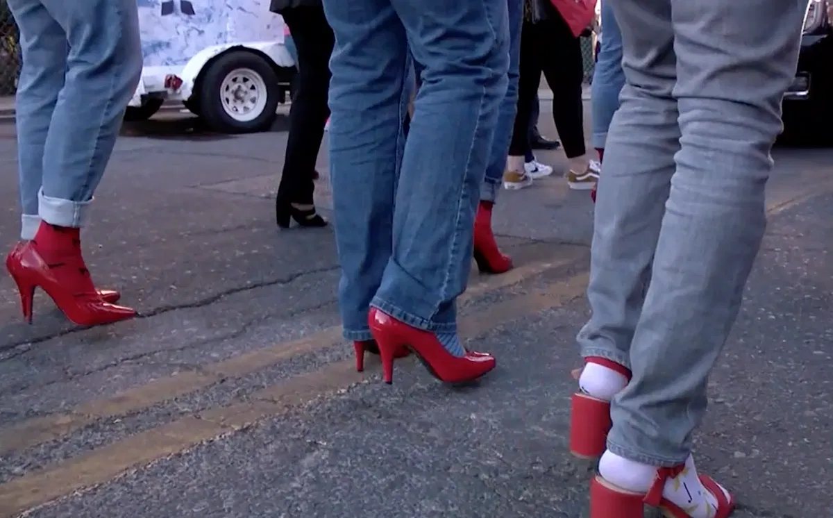 Men walk in red high heels during a Walk a Mile in Her Shoes event