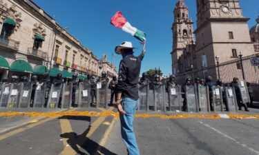 A protester waves a Mexican flag in front of police officers during a demonstration against the assassination of Uruapan's mayor at the Government Palace in Morelia