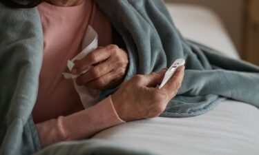 An older woman with the flu checks her temperature using a thermometer.