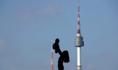 A woman holding up her baby is silhouetted against the backdrop of N Seoul Tower