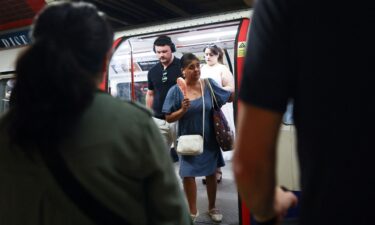 A woman uses an electric fan as she steps out of a train carriage on the London Underground during a heatwave in London