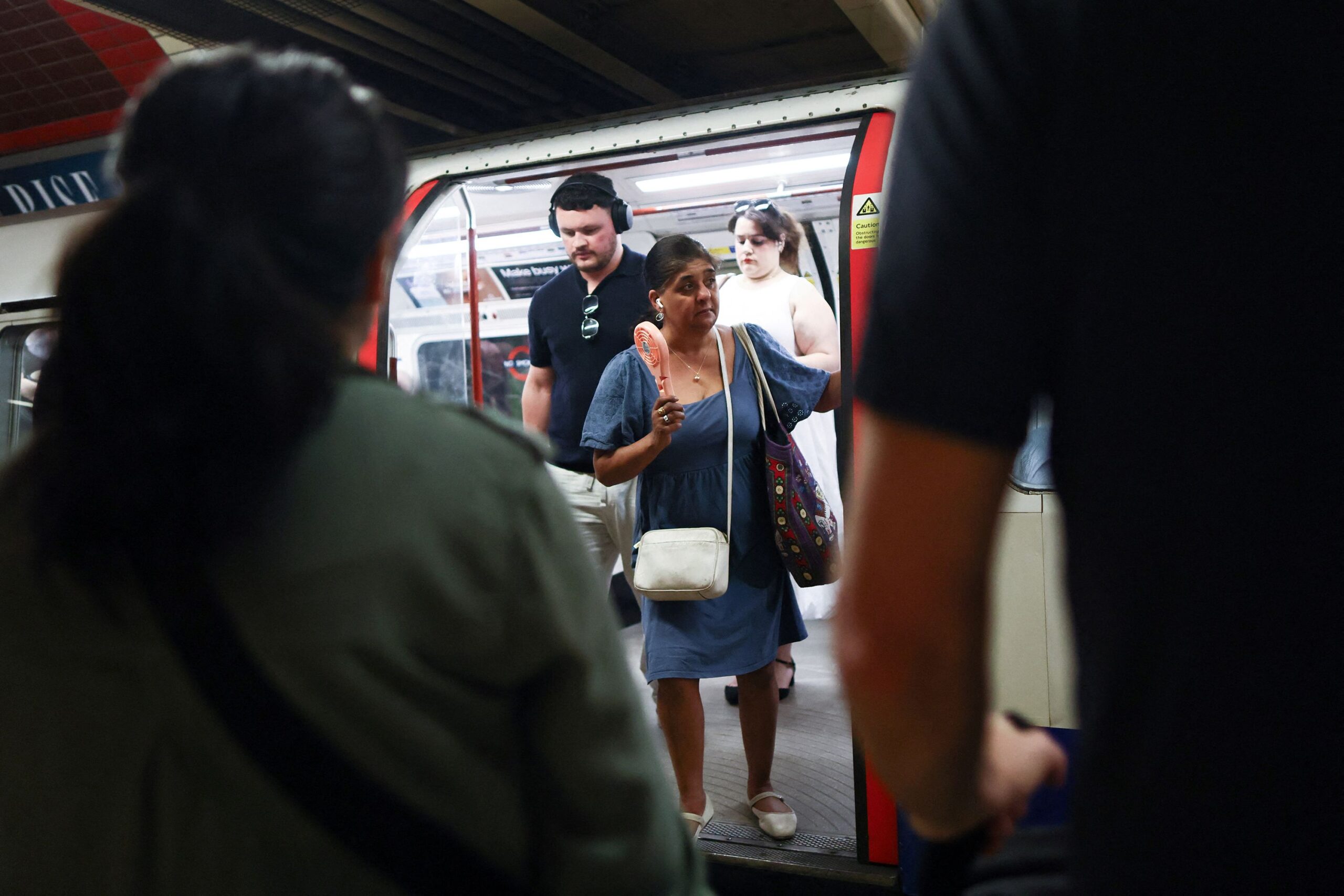 <i>Jack Taylor/Reuters via CNN Newsource</i><br/>A woman uses an electric fan as she steps out of a train carriage on the London Underground during a heatwave in London