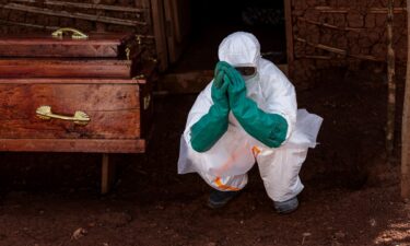 A health worker wearing protective equipment crouches beside the coffin of a suspected Ebola victim during safe burial procedures outside a family home in the community of Mongbwaluon on May 24