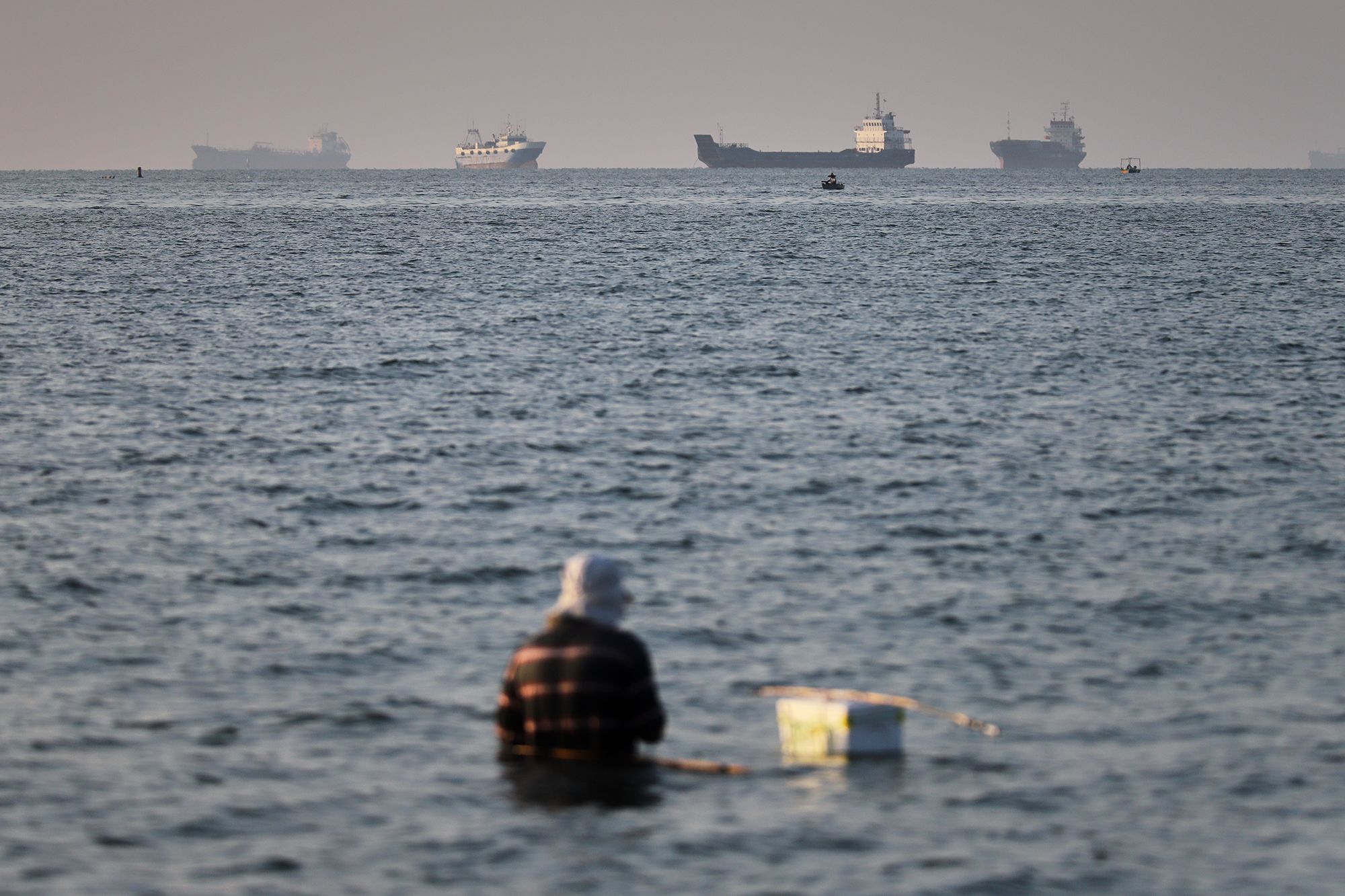 <i>Amirhosein Khorgooi/ISNA/AP via CNN Newsource</i><br/>A person sits in shallow water as cargo and commercial vessels are anchored in the Strait of Hormuz off Bandar Abbas