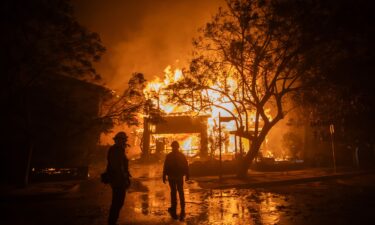 Firefighters watch the flames from the Palisades Fire burning a home on January 8 in Los Angeles.