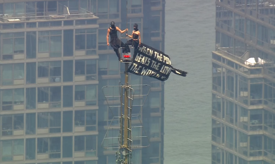 Two people display a banner after climbing to the top of the antenna on the Empire State Building in New York City, July 1, 2026.