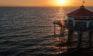 The sun sets over the Pacific Ocean as people gather on Huntington Beach Pier on July 1