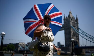 A woman uses an umbrella to shield herself from the sun while walking near Tower Bridge