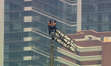 Two people scale to the top of the Empire State Building carrying a pro-peace banner on July 1.