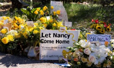 A sign reads stands amid yellow flowers left at the house of Nancy Guthrie