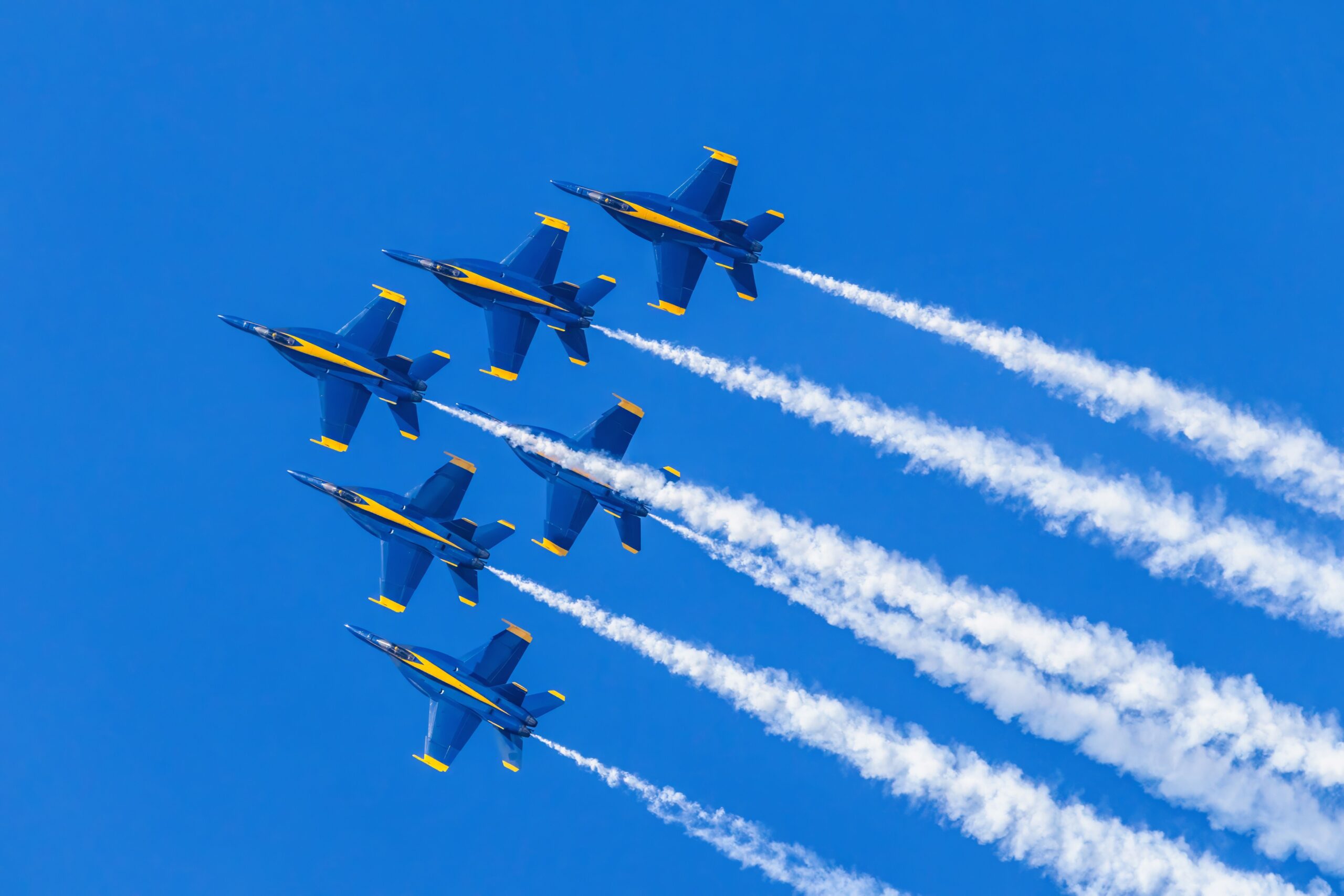 Dynamic aerial display by Blue Angels with smoke trails against a bright blue sky.
(Courtesy: Robert So, Pexels)